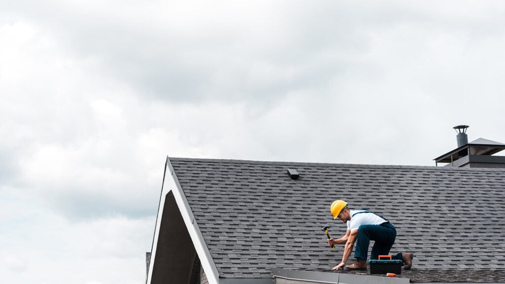 Man fixing the roof of a house, important for curb appeal when selling